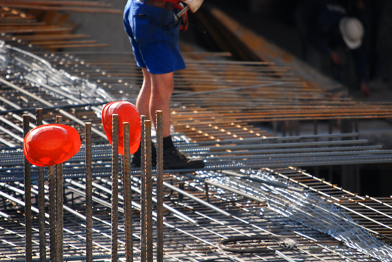 Construction worker standing on steel rebar framework at a building site with safety helmets visible