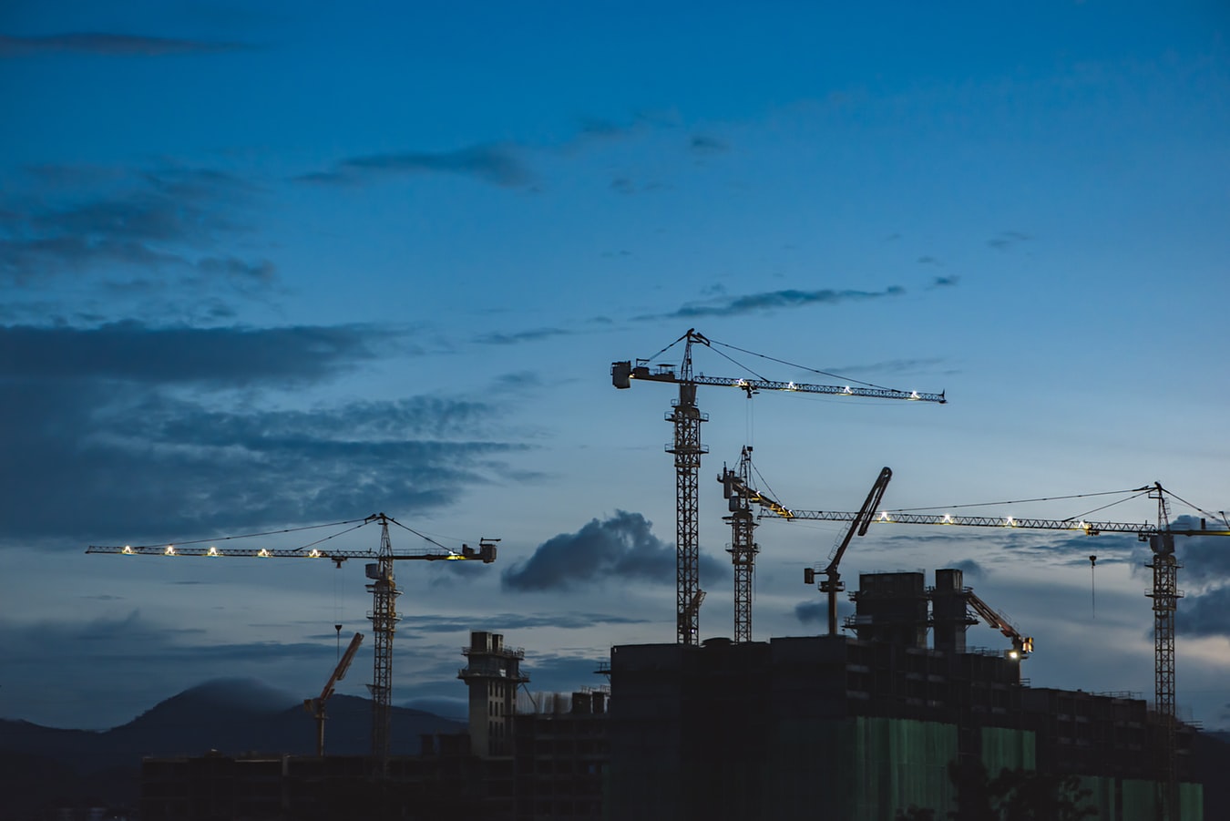 Tower cranes on a construction site against a blue sky, each crane requires documented pre-start and periodic safety inspections
