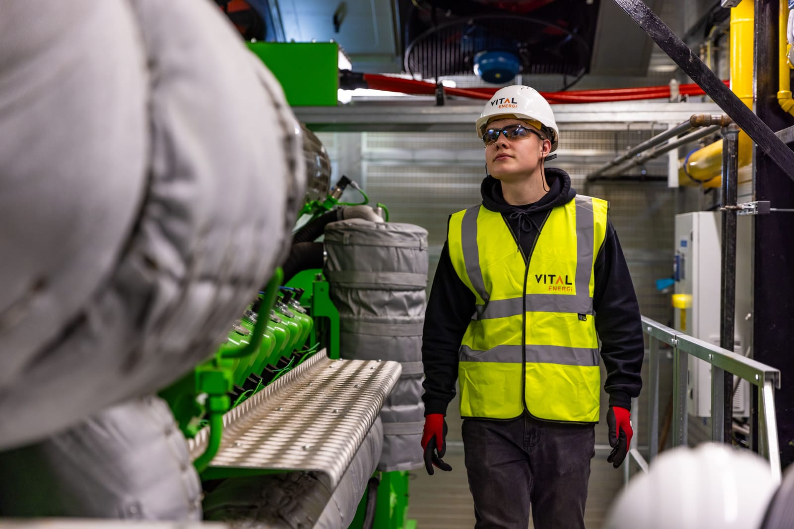 Inspector in a hard hat and high-visibility vest walking through a plant room during an equipment audit