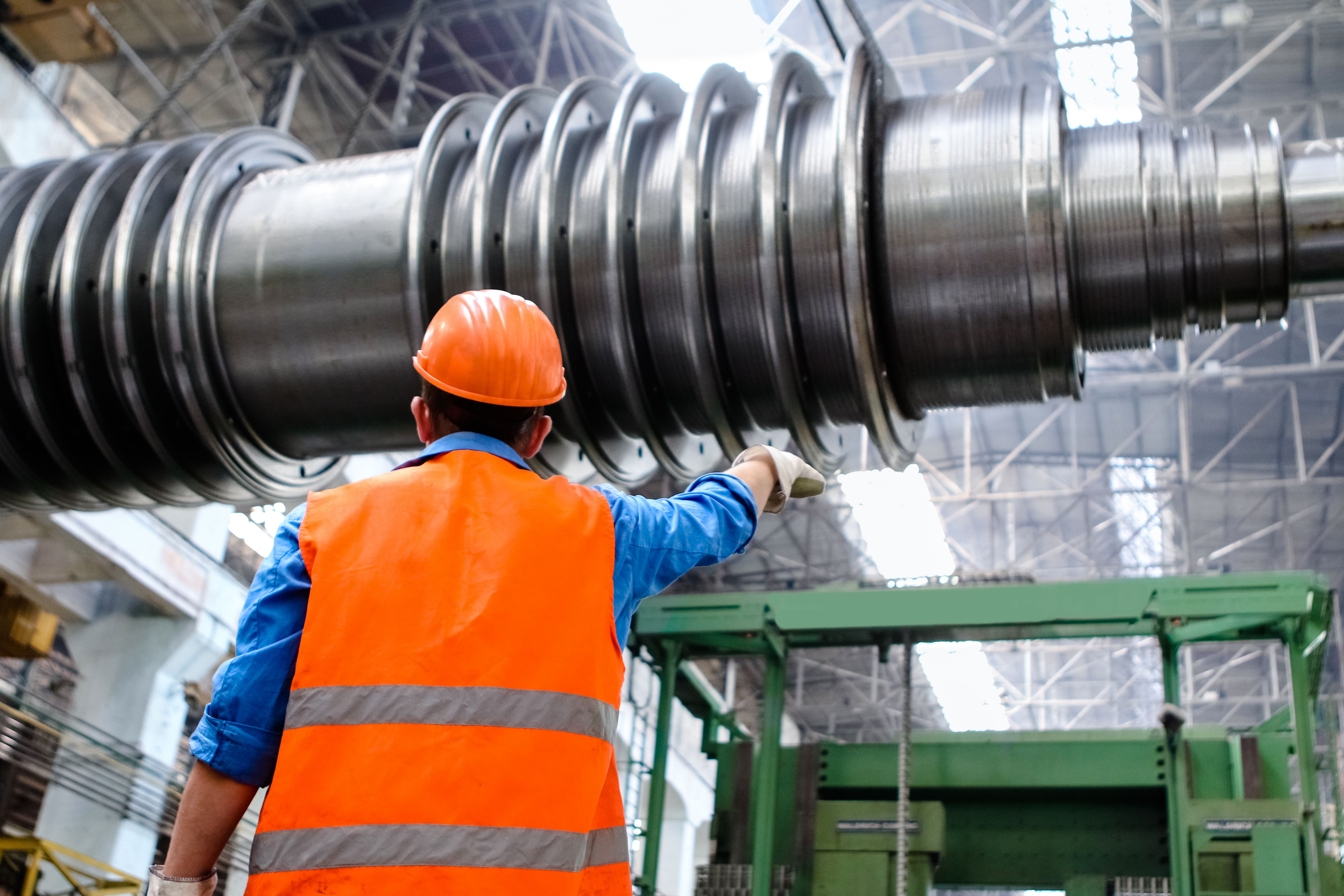 Safety officer in hi-vis and hard hat inspecting large industrial machinery on the factory floor