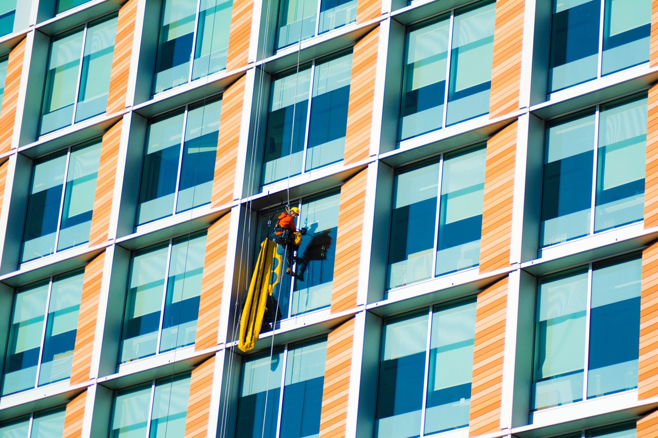 Window cleaner working at height on a high-rise building, representing the safety risks that require rigorous inspection and digital safety planning