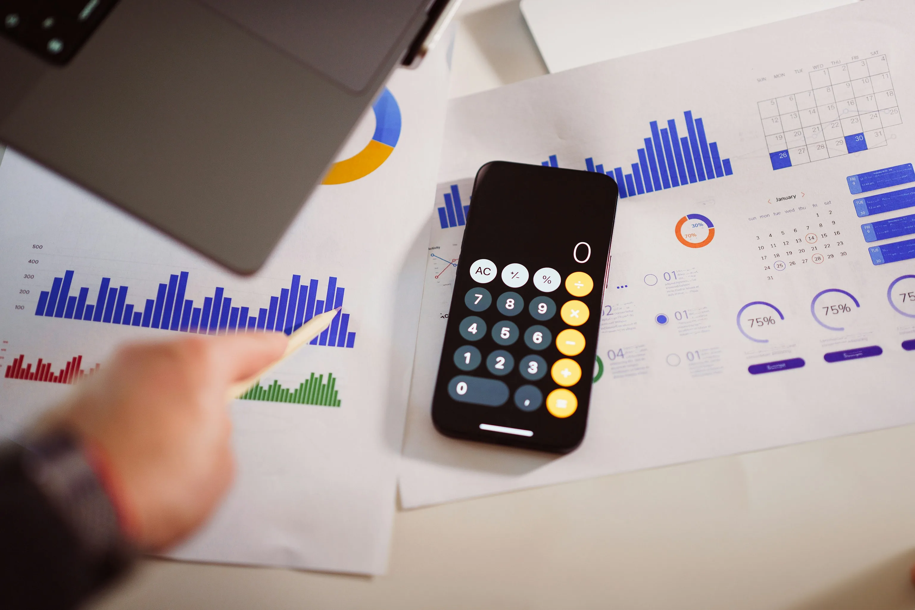 Person reviewing operational cost and performance data on a calculator alongside charts and reports